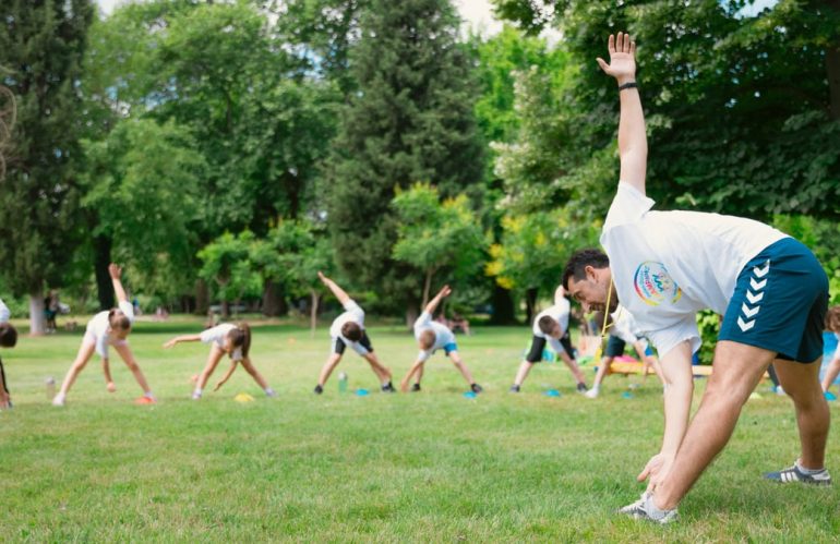 Kids stretching exercises in a park guided by a coach, promoting fitness and fun.