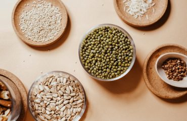 Flat lay of assorted seeds and nuts in rustic saucers on a neutral background, showcasing natural textures.